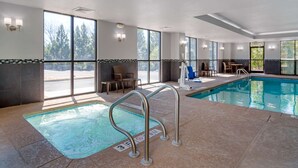Una piscina interior con paredes de vidrio transparente, suelo de baldosas y una escalera de acceso.