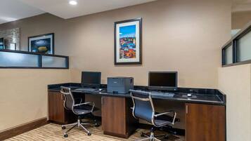 A conference room with three desks, each with a computer and a printer. There are two chairs and a small cabinet. A framed picture hangs on the wall above the desks.