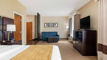 Ein Hotelzimmer mit einem großen Bett, einem Fernseher, einer Couch und einem Schreibtisch mit Lampe.