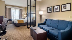 Habitación de hotel con cama, sofá azul, escritorio y silla. Se observan tres cuadros en la pared.