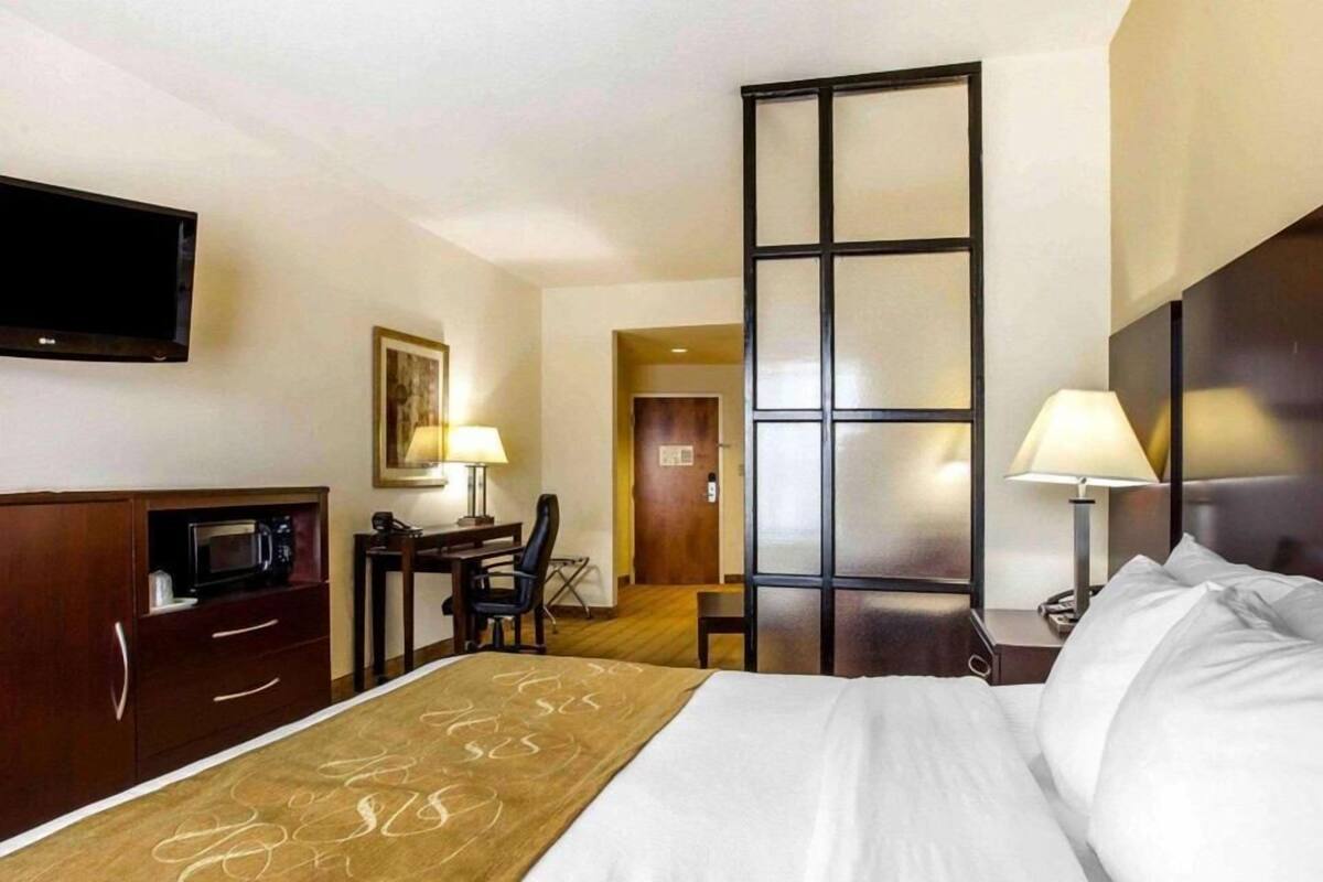 Une chambre d’hôtel comprenant un lit, un bureau, une chaise, une télévision et une porte donnant sur une autre pièce.