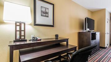 A hotel room with a desk, chair, TV, and framed picture on the wall.