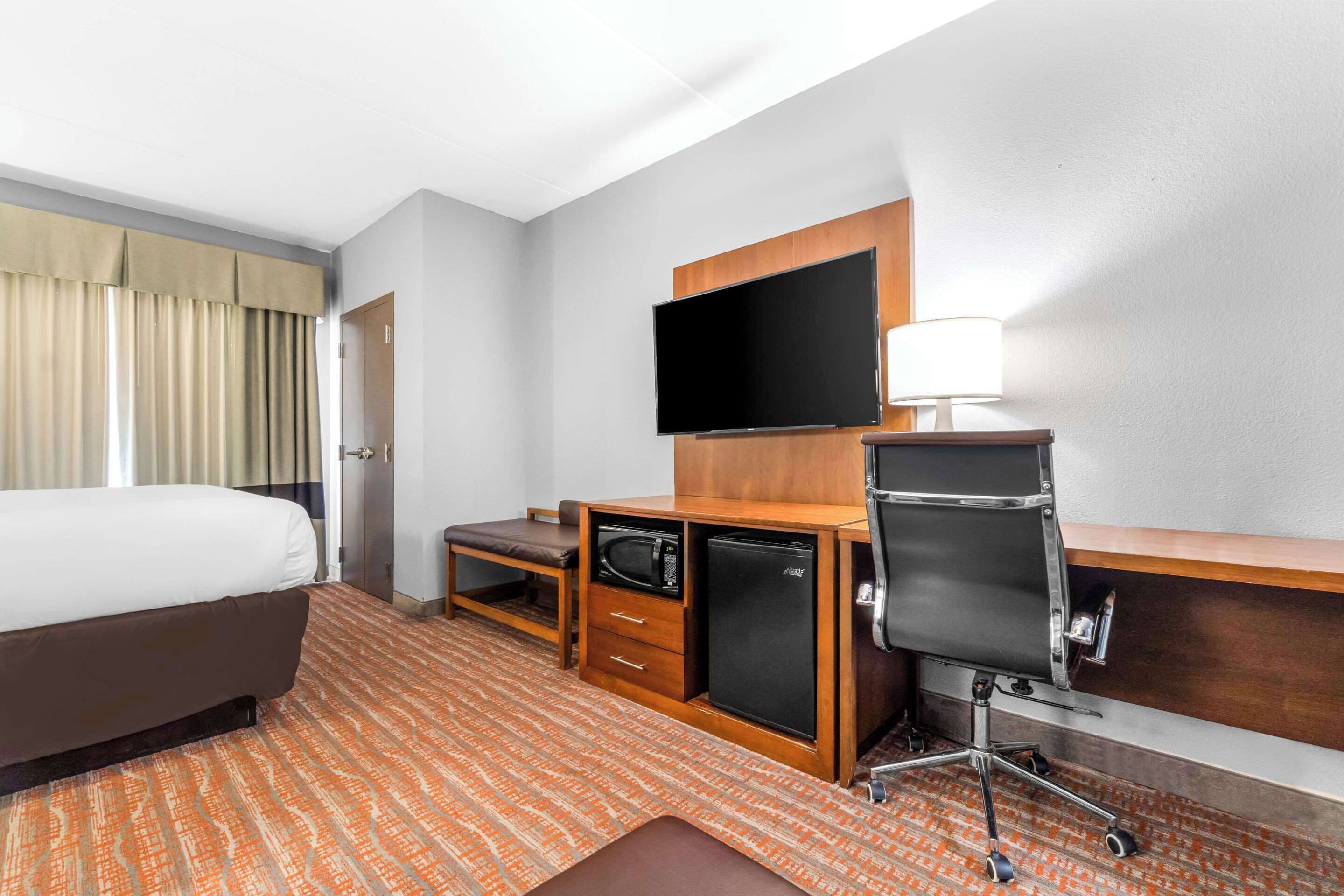 Una habitación de hotel con una cama, un escritorio con computadora, televisor y microondas.