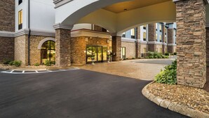 Una entrada de hotel con un vestíbulo techado, columnas de piedra y fachada de ladrillo.