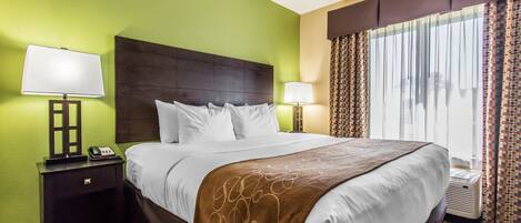A hotel room with a large bed, two bedside tables with lamps, a headboard, and a window with curtains.