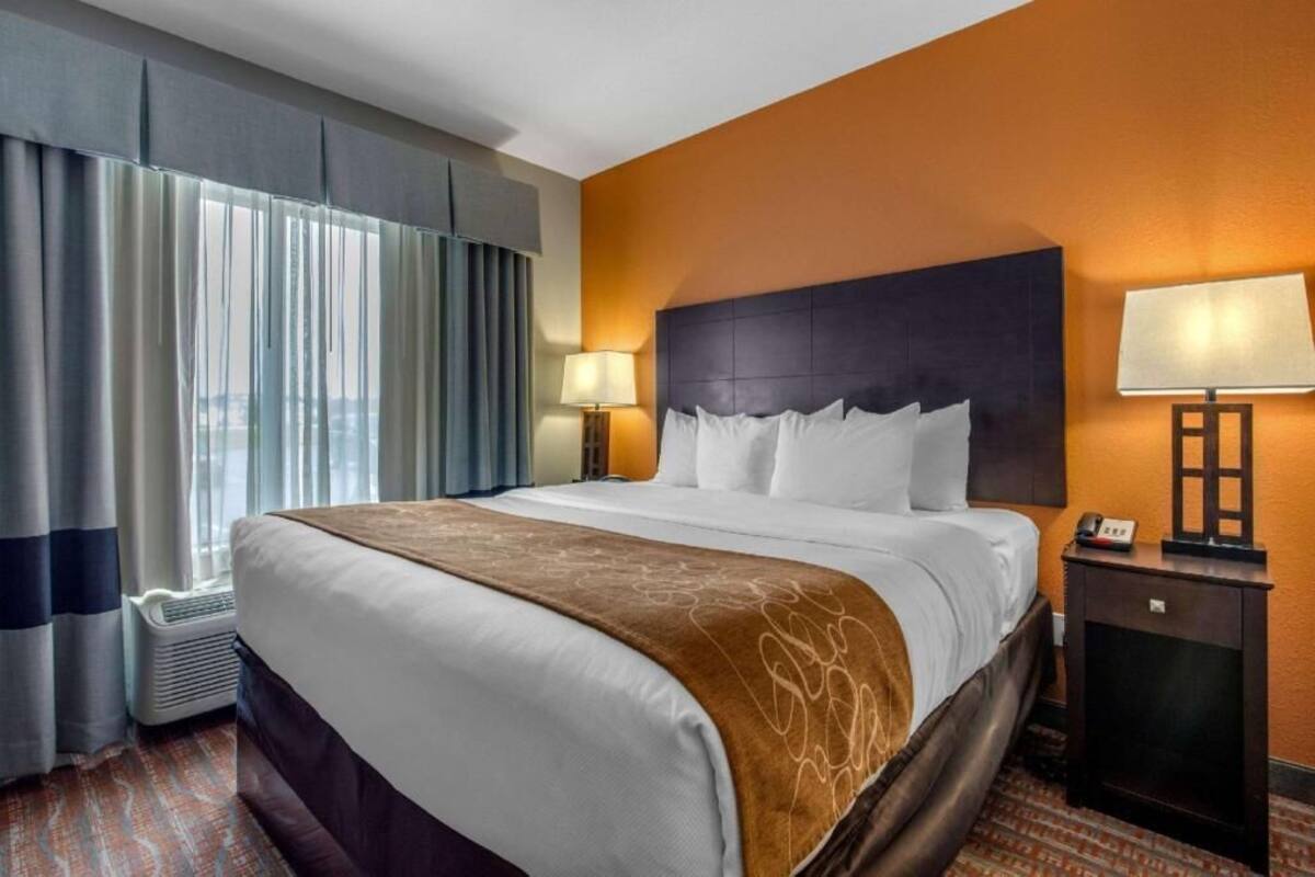 A hotel room with a large bed, two bedside lamps, a nightstand, and a view of the city through the window.