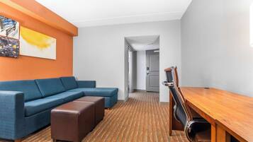 Moderni hotellihuone, jossa on sininen kulmasohva, puinen ruokapöytä ja kuviollinen matto.