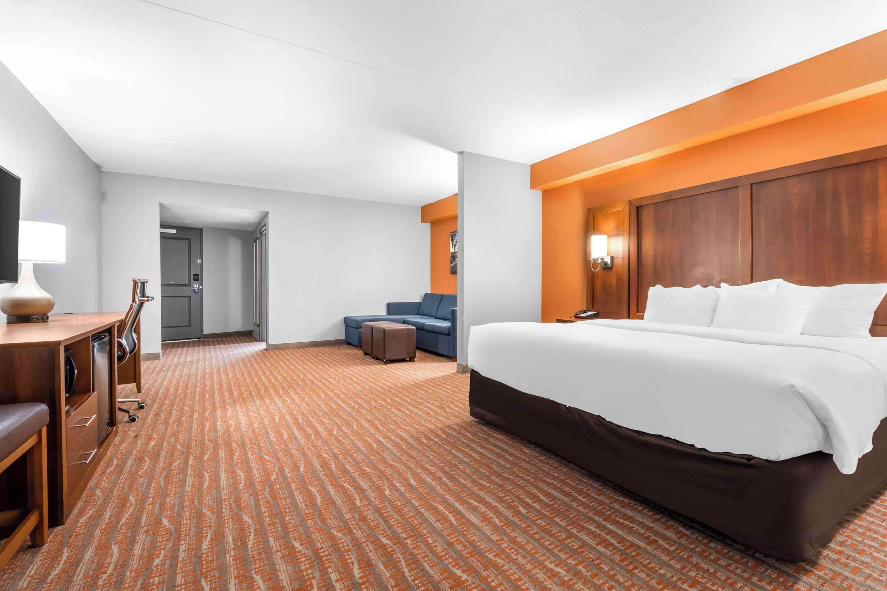 A hotel room with a large bed, a desk with a lamp, a blue sofa, and a patterned carpet.