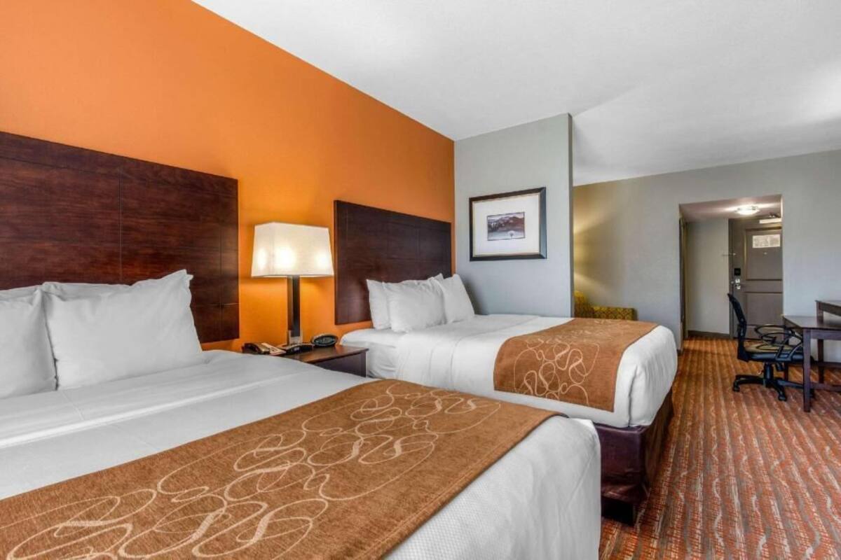 A hotel room with two beds, a desk, a chair, a lamp, and a framed picture on the wall.