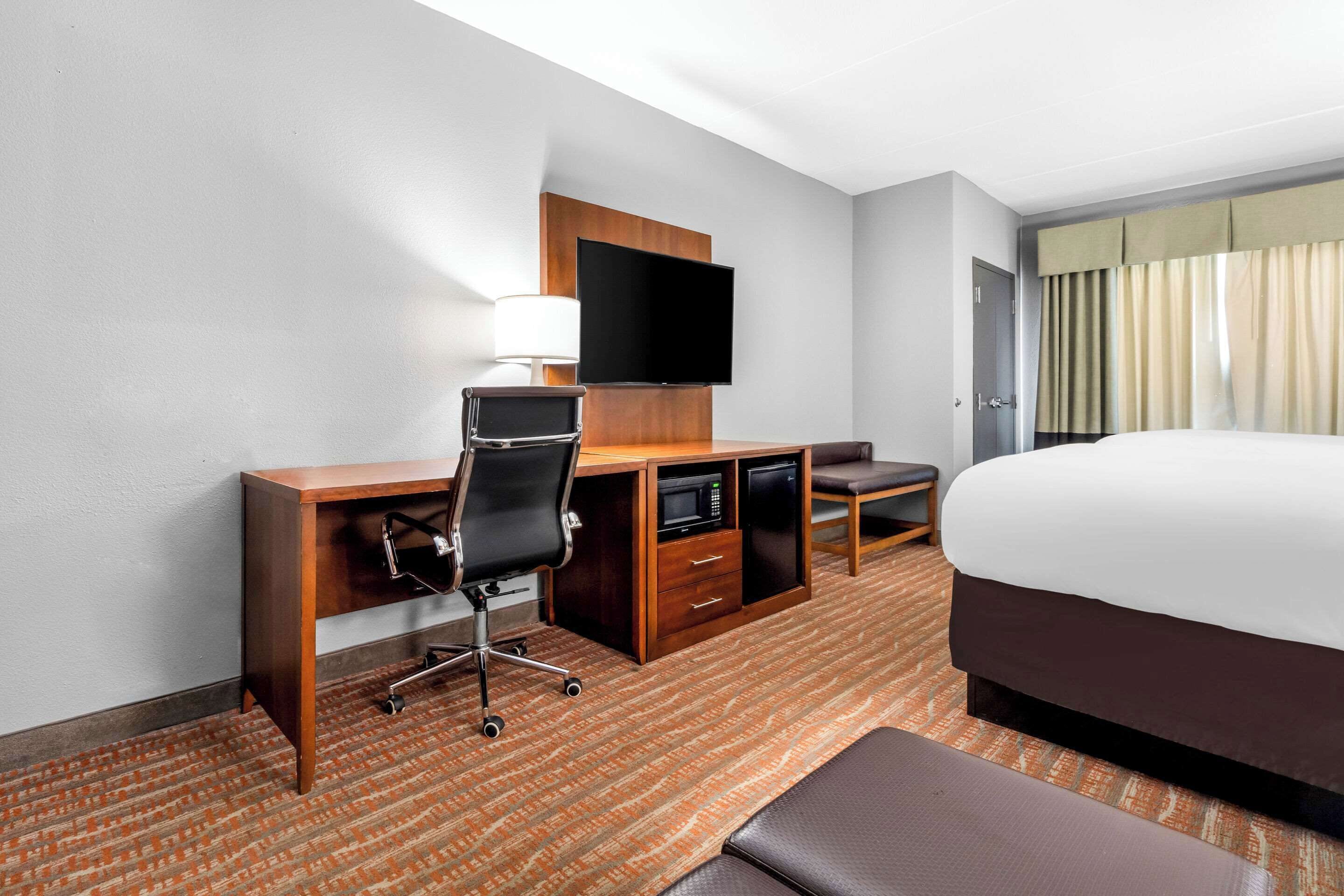 A hotel room with a large bed, a desk with a chair, a flat-screen TV, a microwave, and a small seating area.