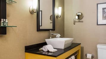 A modern bathroom with a white sink, a mirror, and two wall-mounted lights. There is a toilet paper holder and a towel rack visible.