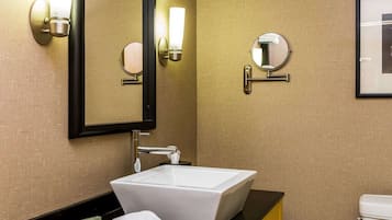 Un baño con un lavabo blanco tipo pedestal, una encimera negra, un armario amarillo, un espejo con apliques de pared, un espejo redondo y un inodoro.