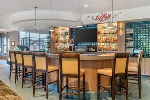 A bar area with a counter, bar stools, and a large screen. - Cambria Hotel Traverse City (Traverse City)