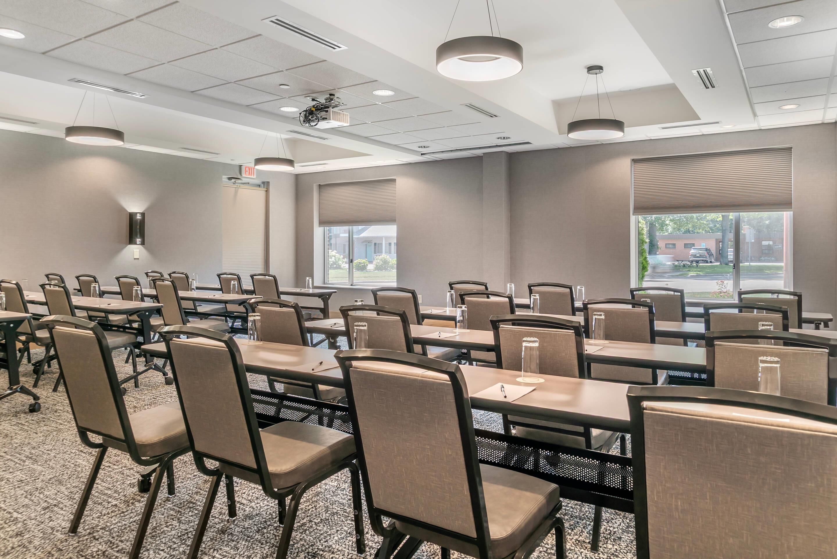 A conference room with multiple tables and chairs, large windows, and ceiling-mounted projectors.