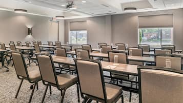 A conference room with multiple tables and chairs, large windows, and ceiling-mounted projectors.