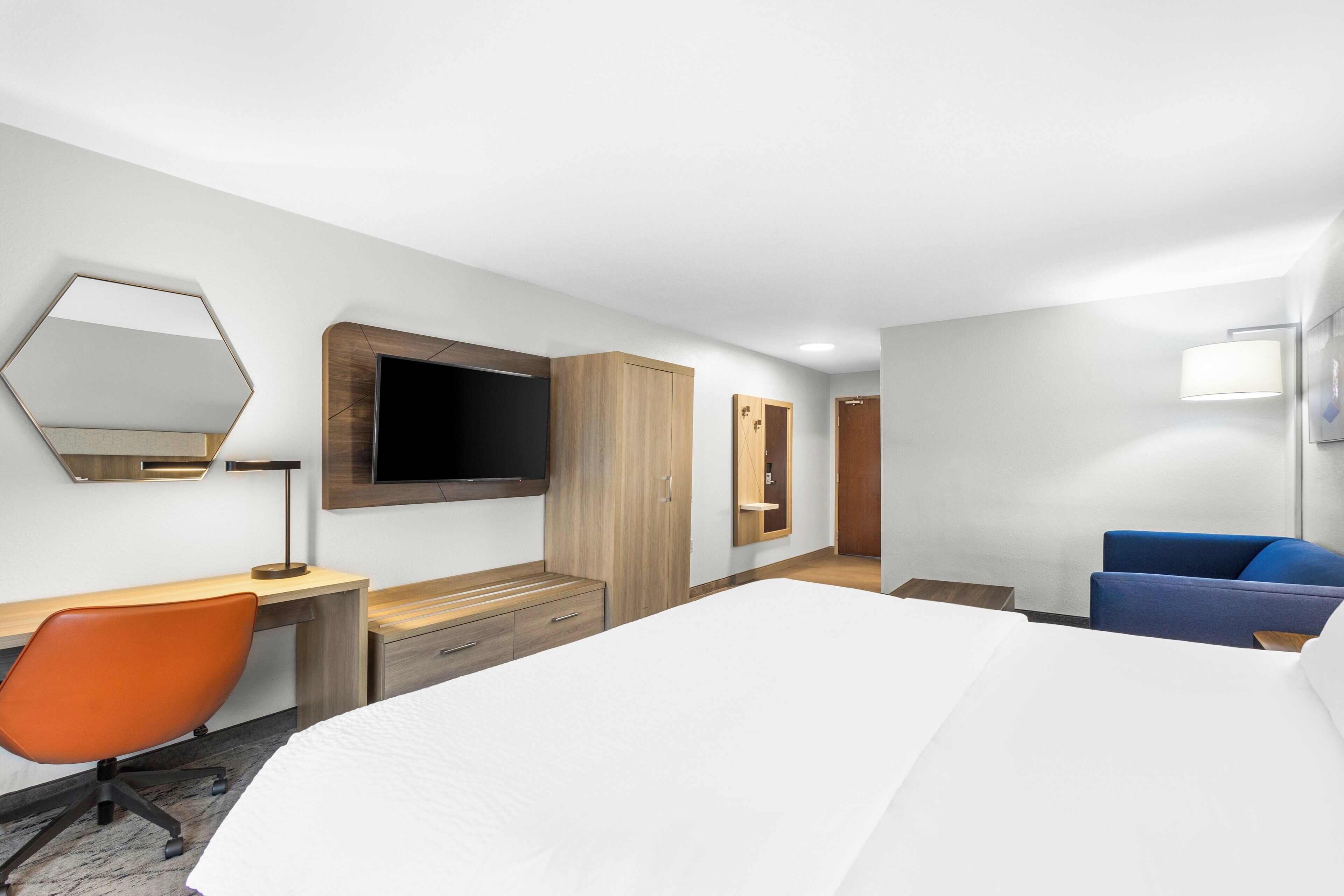 A hotel room with a bed, desk, chair, TV, wardrobe, and a bathroom.