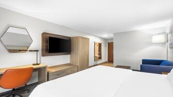 A hotel room with a bed, desk, chair, TV, wardrobe, and a bathroom.