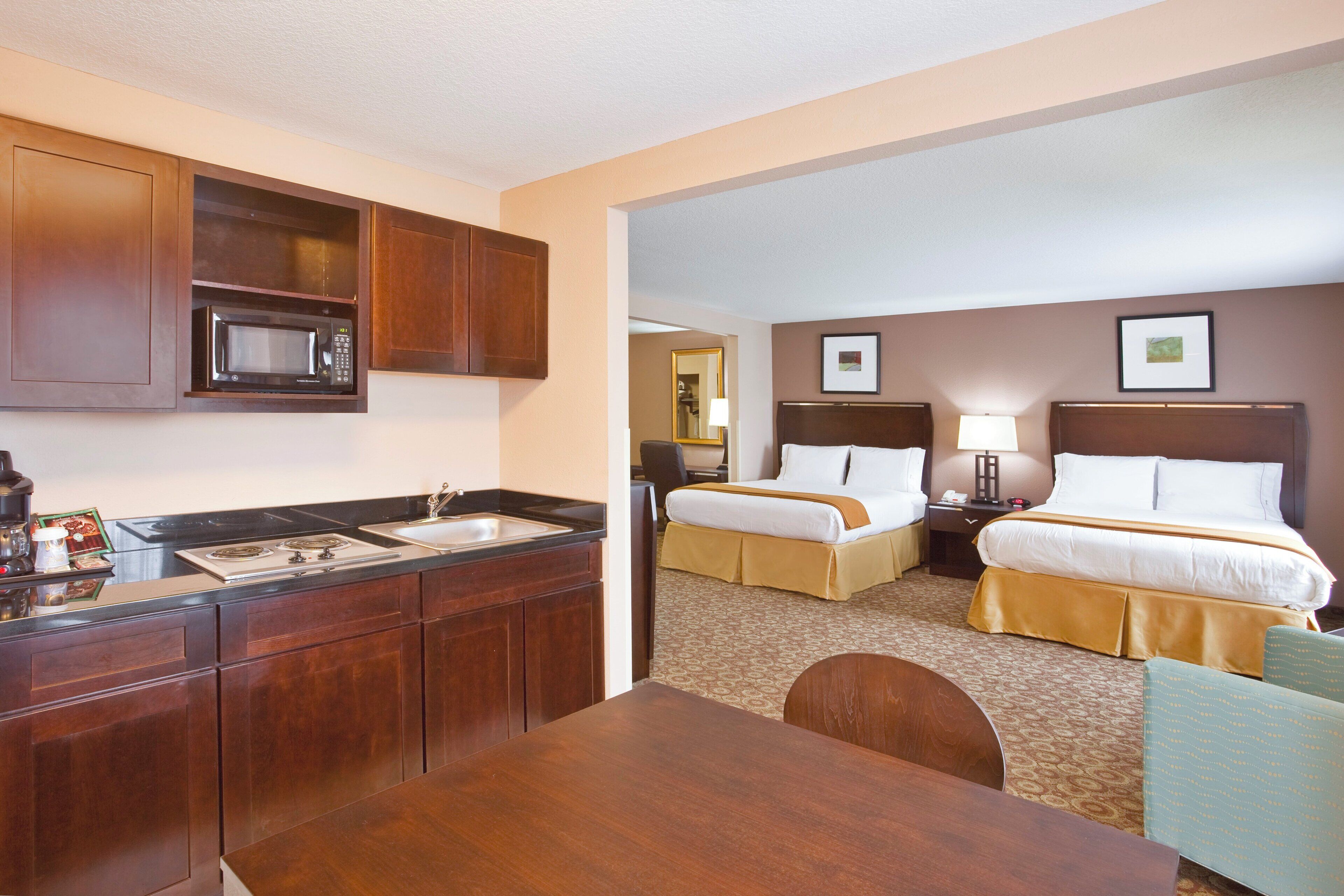 A hotel room with a kitchenette, two beds, a bathroom, and a dining area.