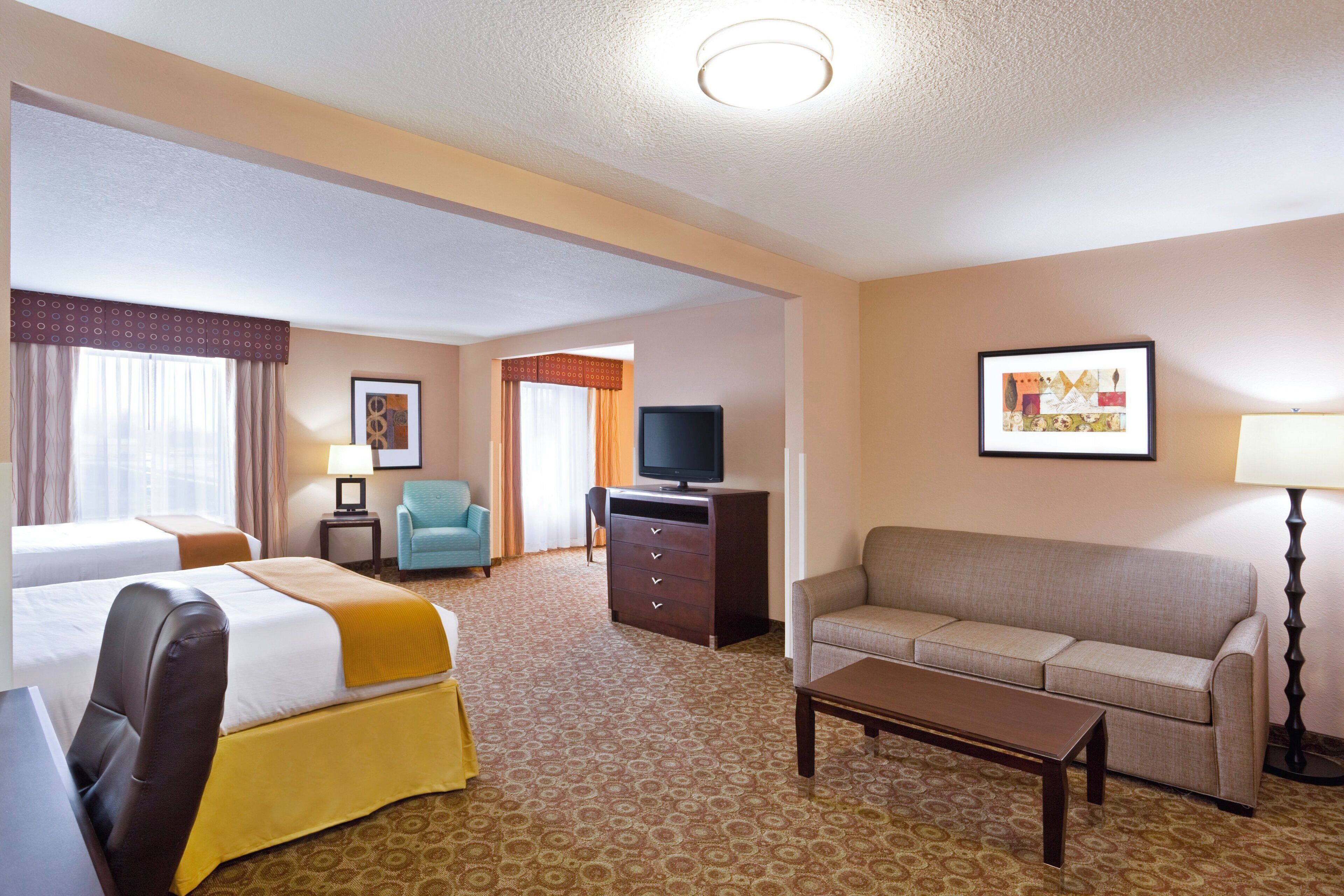 Quarto de hotel com duas camas, um sofá, uma televisão, uma escrivaninha e um quadro na parede.