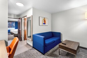 A hotel room with a blue sofa, a small wooden table, and a painting on the wall.