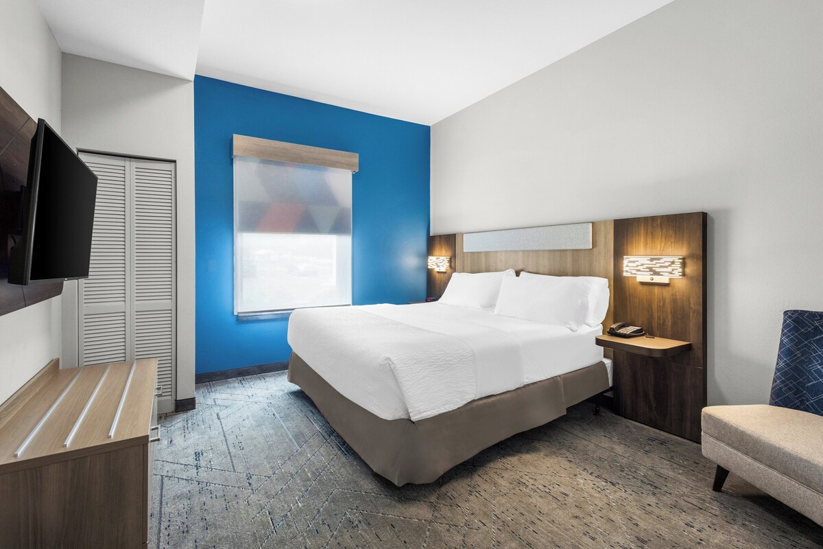 A modern hotel room with a bed, bedside table, lamp, and a television.