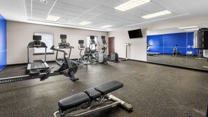 Un gimnasio con máquinas de cardio, una banca y un espejo grande.