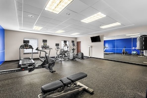 Un gimnasio con máquinas de cardio, una banca y un espejo grande.