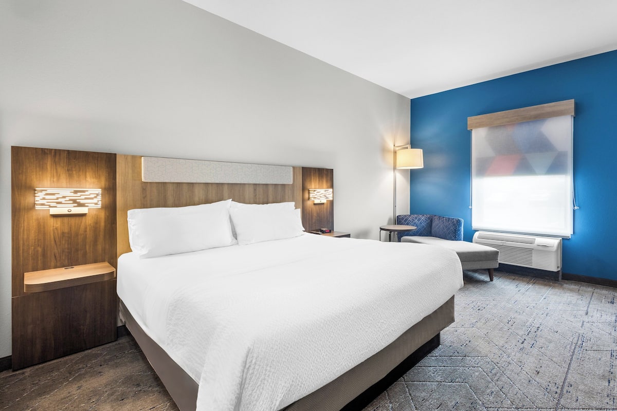 Una habitación de hotel moderna con una cama grande, cabecera de madera, lámparas de noche, una mesita y una pared azul decorativa.