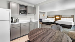 Habitación de hotel moderna con kitchenette, dos camas, una mesa de comedor y vistas a la ciudad.