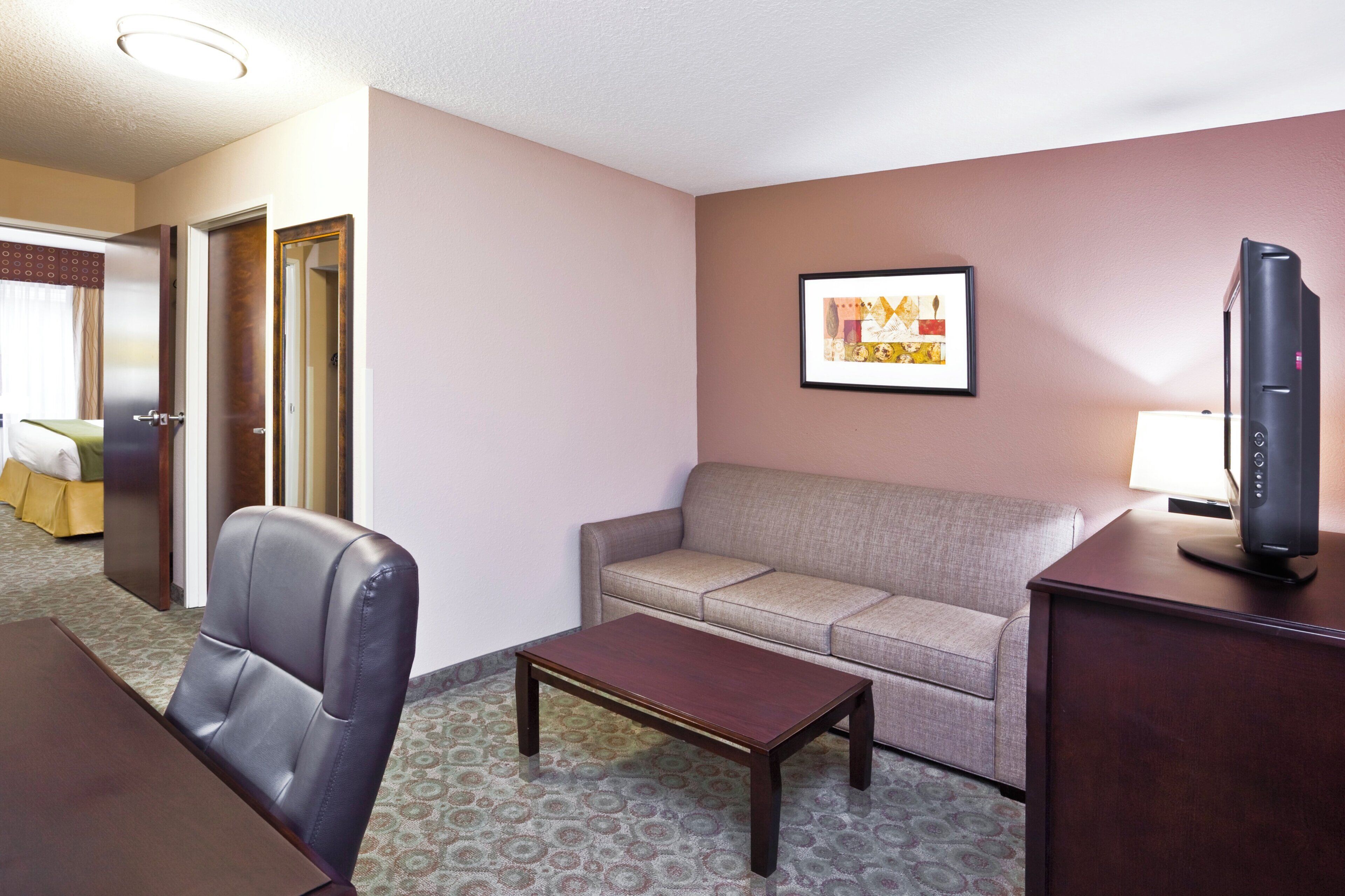A hotel room with a sofa, a chair, a small table, a television, and a framed picture on the wall.