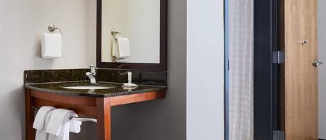 A hotel bathroom with a sink, mirror, towel rack, and a door leading to a shower area.