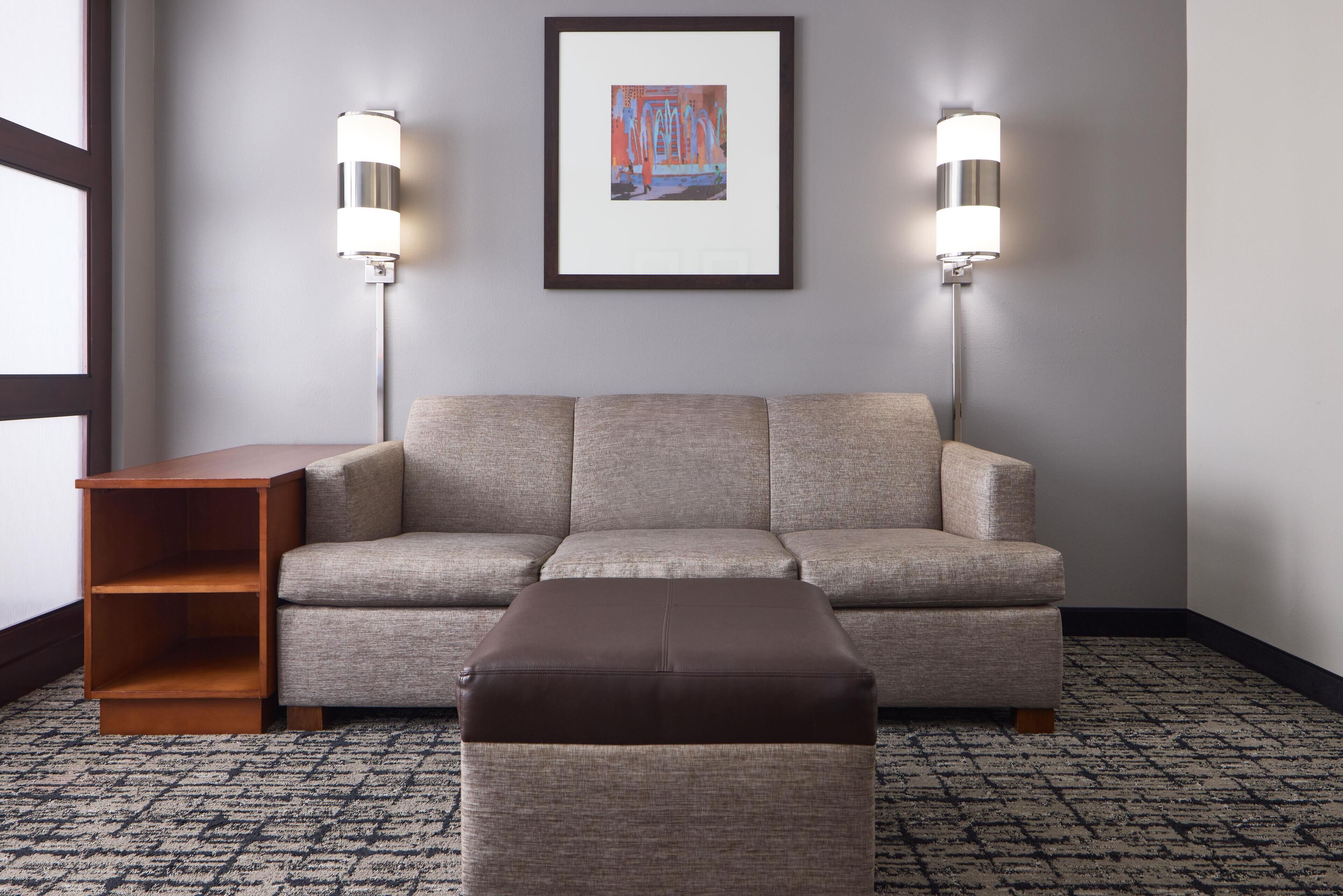 A neutral-toned sofa with a matching ottoman, a wooden side table, and two wall-mounted lamps.