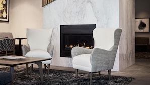 A modern living room with a fireplace, two armchairs, a coffee table, and a patterned rug. - Hyatt Place Salt Lake City/Downtown/The Gateway (Salt Lake City)