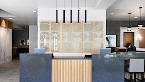 A modern reception desk with a wooden panel design, two laptops, and a seating area with a chair. - Hyatt Place Salt Lake City/Downtown/The Gateway (Salt Lake City)