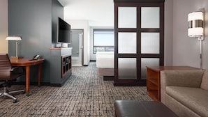 A hotel room with a flat-screen TV, a desk with a lamp, a sofa, a bed, and a sliding door to a balcony. - Hyatt Place Salt Lake City/Downtown/The Gateway (Salt Lake City)