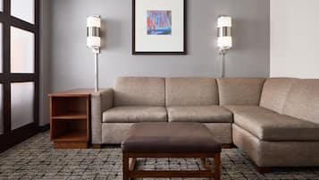 A living room with a beige sectional sofa, a wooden bench, two wall-mounted floor lamps, and a framed abstract painting on the wall.