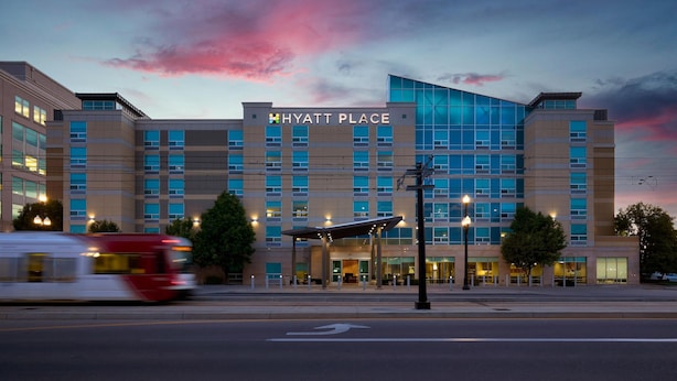 A modern Hyatt Place hotel with a prominent glass facade, a covered entrance, and a red bus in motion. - Hyatt Place Salt Lake City/Downtown/The Gateway (Salt Lake City)