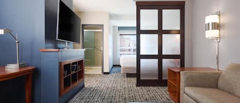 A hotel room with a flat-screen TV, a wooden side table, a sofa, a large window, and a sliding door.