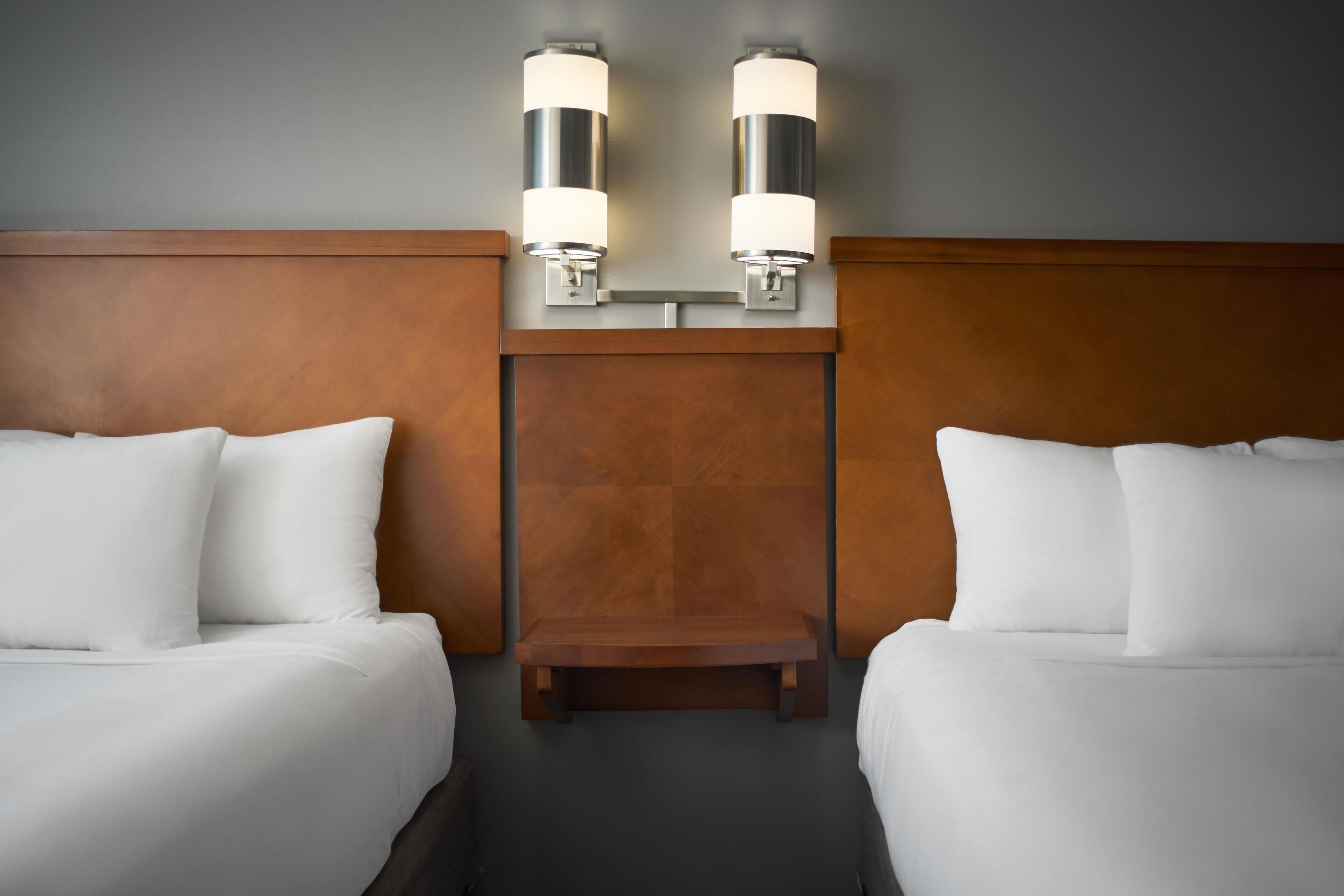 A hotel room with two beds, a wooden headboard, and wall-mounted sconces.