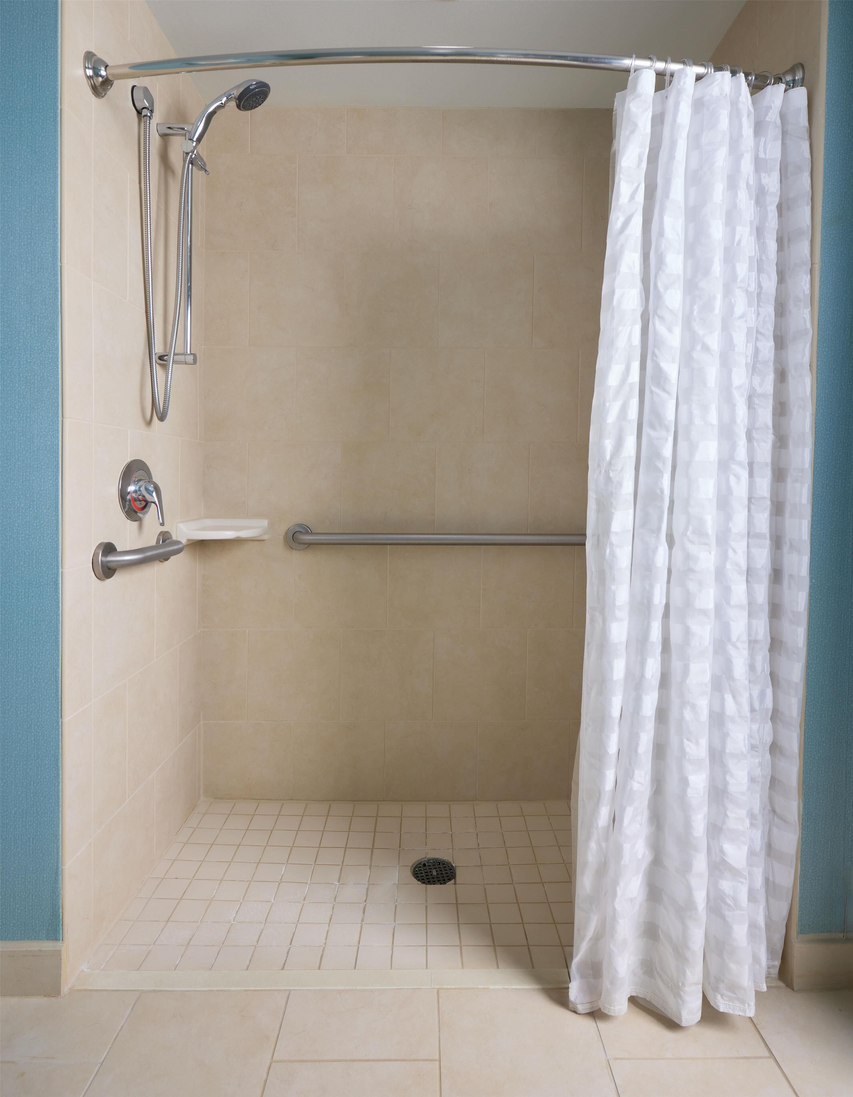 A shower area with a white curtain, a handheld showerhead, a wall-mounted faucet, and a grab bar.