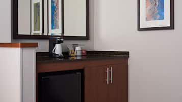 A hotel reception area with a dark wood cabinet, a coffee machine, a refrigerator, and framed artwork on the wall.