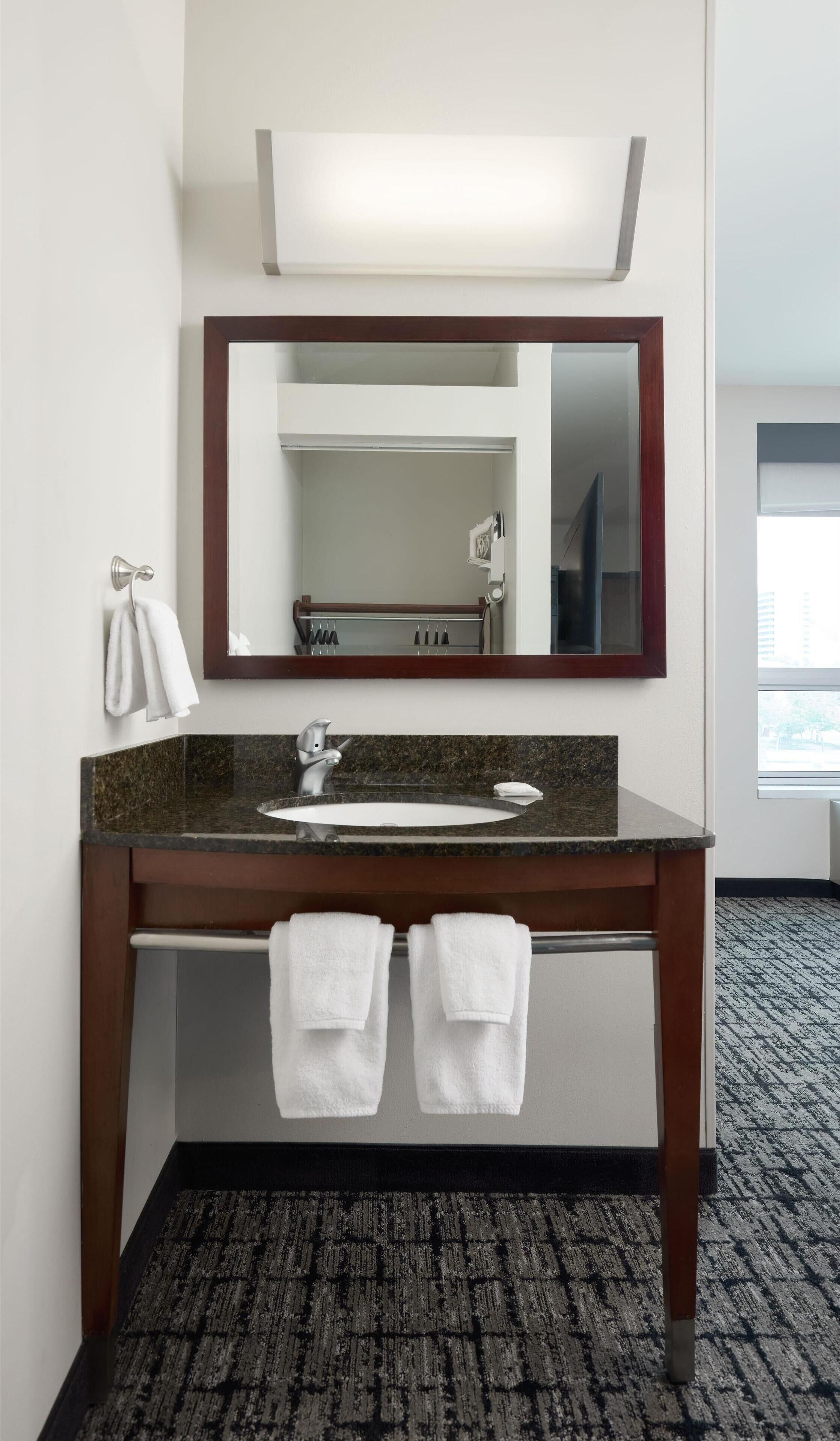 A hotel bathroom with a marble sink, a mirror, and two towels hanging on the wall.
