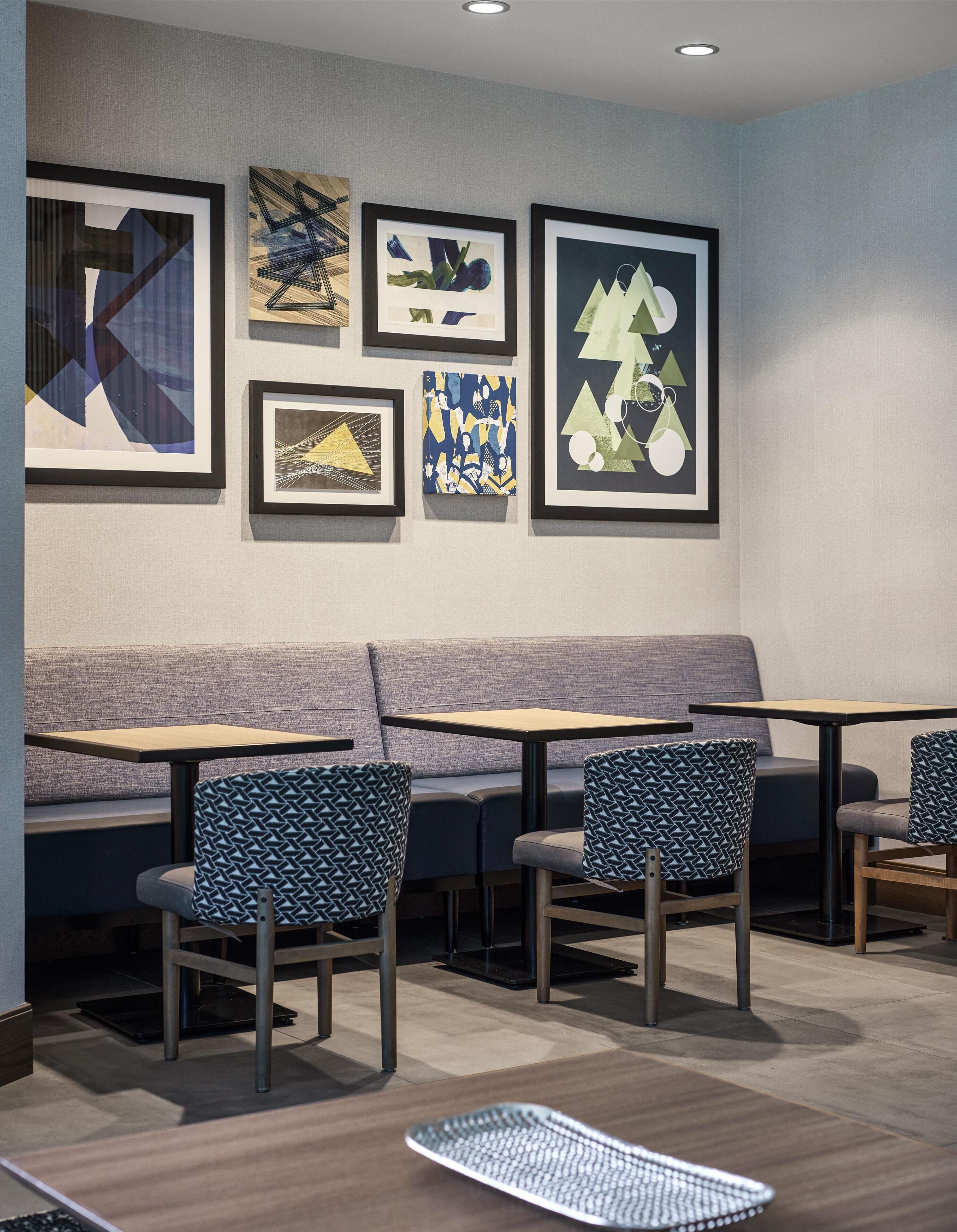 Un café moderne avec un canapé et des tables, des œuvres d’art encadrées au mur et des chaises à motifs.