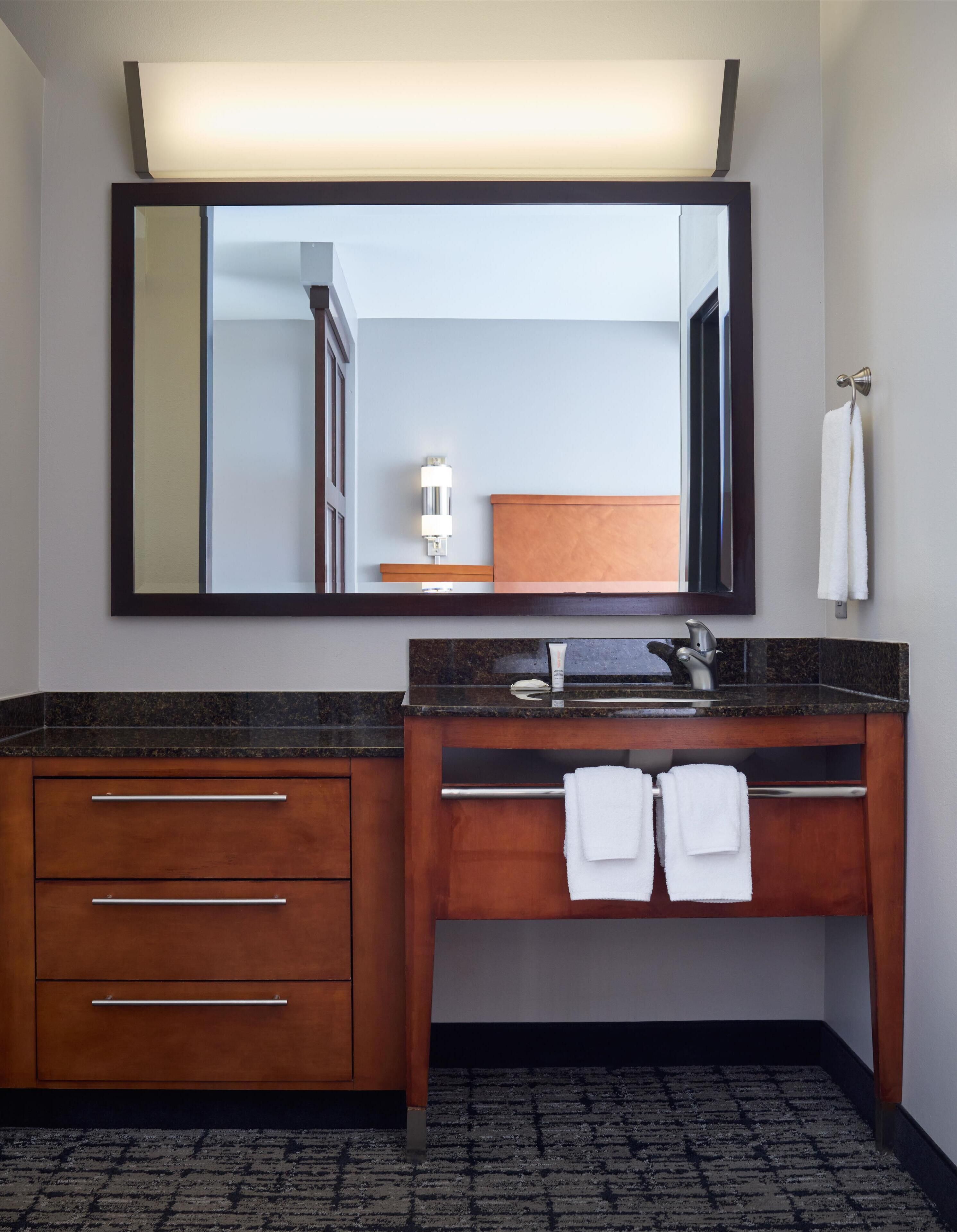 A modern bathroom with a large mirror, wooden vanity, two sinks, and a towel rack.