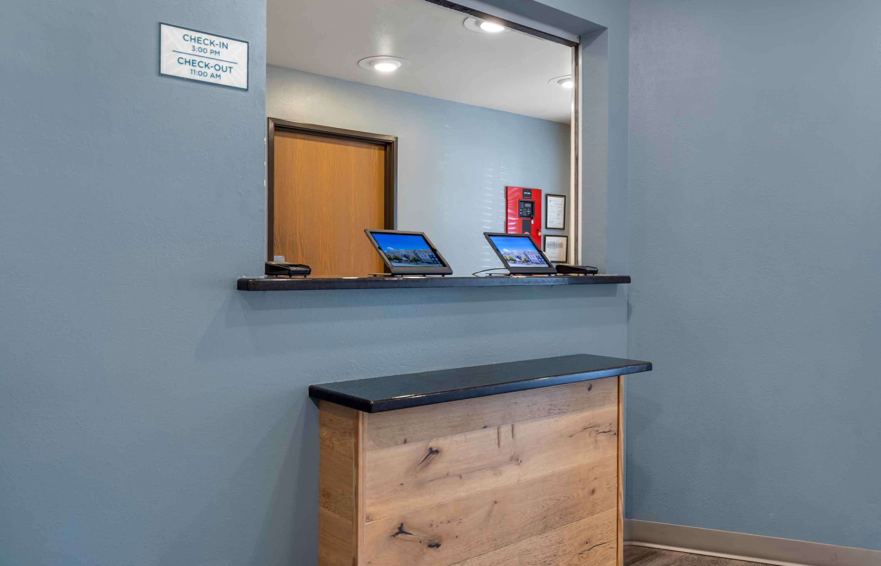 A reception desk with a mirror, two laptops, and a sign indicating check-in and check-out times.