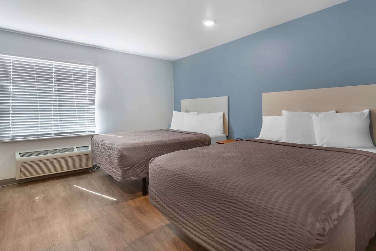 A hotel room with two beds, a window with blinds, a heater, and a blue wall.