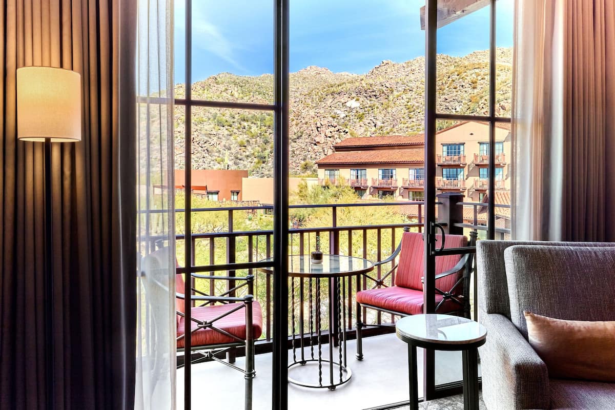 A balcony with a view of a mountainous landscape, furnished with a sofa, chairs, and a small table.