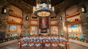 A spacious dining area with a large round table set for multiple guests, surrounded by stone walls and wooden beams.