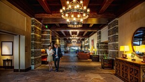 A spacious lobby with stone flooring, a grand chandelier, and a reception desk.