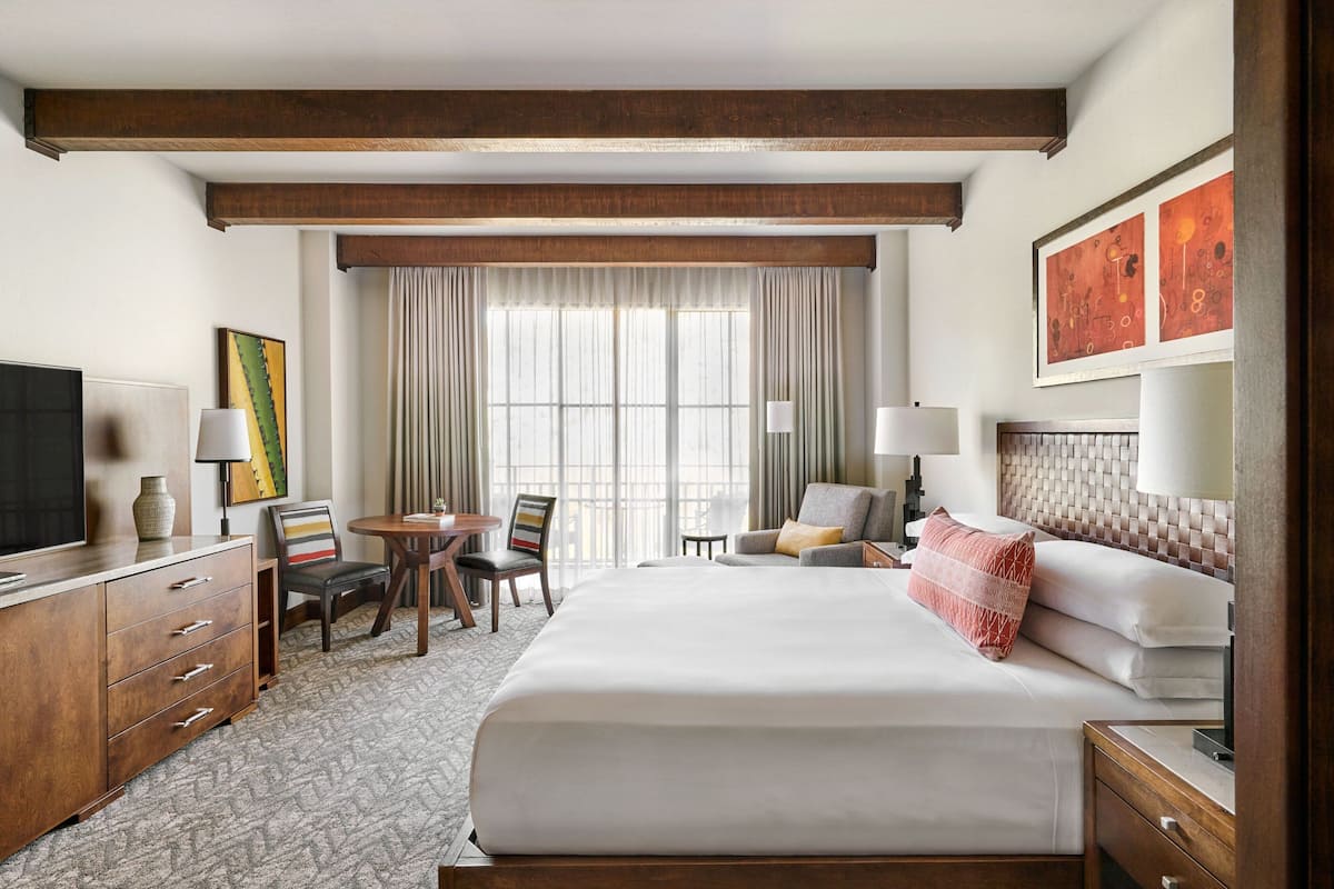 A hotel room with a large bed, a desk, a chair, a TV, and a window with curtains.